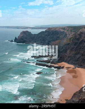Sandstrand mit felsigen Bergrücken trübes Wetter Aussicht auf Sommer Atlantic an der felsigen Küste (Costa Vicentina, Algarve, Portugal). Und Ocean Surf Wellen. Stockfoto