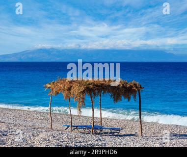 Sommer morgen kiesiger Strand mit Sonnenliegen und Baldachin (Albanien). Stockfoto