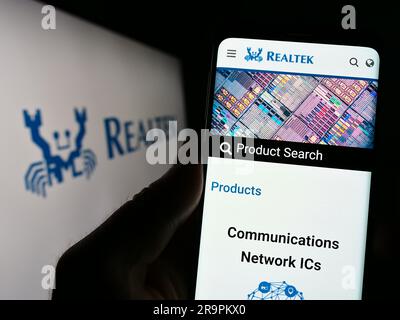 Person, die ein Handy hält, mit Webseite der taiwanesischen Firma Realtek Semiconductor Corp. Auf dem Bildschirm mit Logo. Konzentrieren Sie sich auf die Mitte des Telefondisplays. Stockfoto