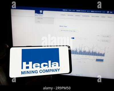 Person, die ein Mobiltelefon mit dem Logo des amerikanischen Unternehmens Hecla Mining Company auf dem Bildschirm vor der Webseite hält. Konzentrieren Sie sich auf das Display des Telefons. Stockfoto