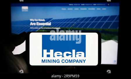 Person, die ein Mobiltelefon mit dem Logo des US-amerikanischen Unternehmens Hecla Mining Company auf dem Bildschirm vor der Webseite hält. Konzentrieren Sie sich auf das Display des Telefons. Stockfoto