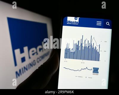 Person, die ein Mobiltelefon mit einer Webseite des US-amerikanischen Unternehmens Hecla Mining Company auf dem Bildschirm vor dem Logo hält. Konzentrieren Sie sich auf die Mitte des Telefondisplays. Stockfoto