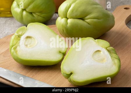 Ganze und halbierte frische Chayote auf einem Schneidebrett, Nahaufnahme Stockfoto