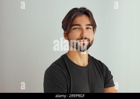 Porträt eines gutaussehenden, lächelnden jungen Mannes mit gefalteten Armen. Ein lächelnder, fröhlicher Mann mit einem kreuzenden Studiofoto. Isoliert auf grauem Hintergrund. Porträt von y Stockfoto
