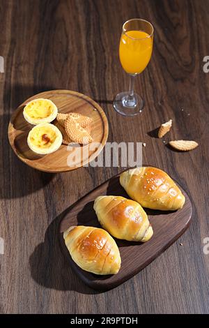 Ein herrliches Frühstücksambiente mit mehreren Croissants und einem Glas frisch gepressten Orangensaft auf einem Holztisch Stockfoto