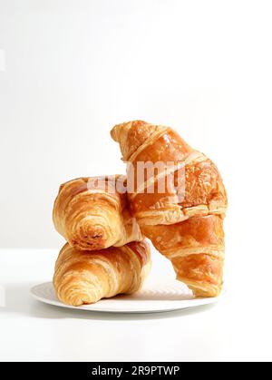 Drei frisch gebackene Croissants auf einem weißen Teller mit weißem Hintergrund Stockfoto