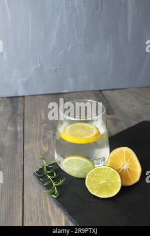 Wasser mit Zitrone hausgemachte Limonade in einem Glas daneben gibt es Zitronen mit Kräutergrünem Rosmarin auf einem schwarzen Stand mit einem Platz für Text. Gesundes Essen Stockfoto