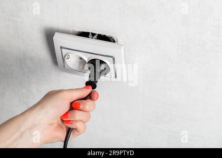 Das Mädchen zieht fälschlicherweise den Stecker aus der Steckdose und unterbricht die Steckdose. Stromschlaggefahr. Platz für Text kopieren Stockfoto