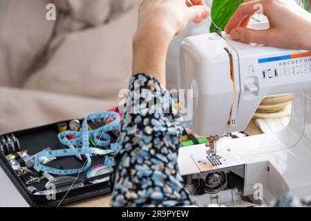 Die Hand einer Frau näht Tümpel an eine elektrische Nähmaschine. Füllung des Fadens in die Nähnadel, Einstellung der Spannung. Komfort im Haus, a h Stockfoto