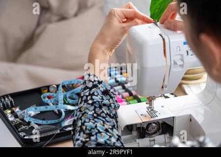 Die Hand einer Frau näht Tümpel an eine elektrische Nähmaschine. Füllung des Fadens in die Nähnadel, Einstellung der Spannung. Komfort im Haus, a h Stockfoto