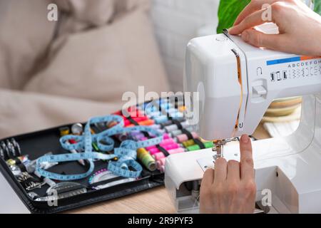 Die Hand einer Frau näht Tümpel an eine elektrische Nähmaschine. Füllung des Fadens in die Nähnadel, Einstellung der Spannung. Komfort im Haus, a h Stockfoto