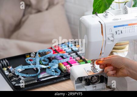 Die Hand einer Frau näht Tümpel an eine elektrische Nähmaschine. Füllung des Fadens in die Nähnadel, Einstellung der Spannung. Komfort im Haus, a h Stockfoto