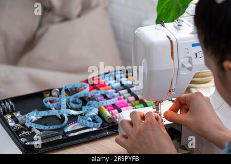 Die Hand einer Frau näht Tümpel an eine elektrische Nähmaschine. Füllung des Fadens in die Nähnadel, Einstellung der Spannung. Komfort im Haus, a h Stockfoto