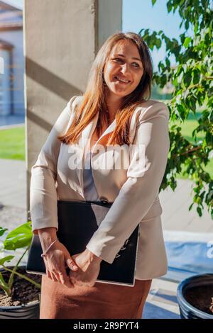 Selbstbewusster Unternehmer im Anzug, der den Laptop am Fenster hält. Weiße junge Geschäftsfrau, die in einem modernen Büro am Fenster steht. Stockfoto