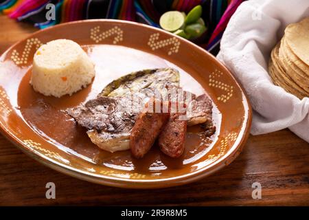 Geröstetes Fleisch mit geröstetem Nopalkaktus und Schweinewürstchen namens Chorizo, begleitet von weißem Reis, serviert auf einem typisch mexikanischen Tonteller. Stockfoto