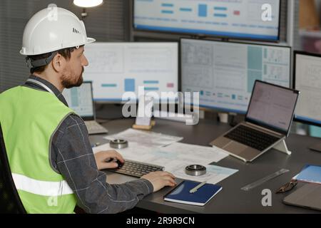 Rückansicht eines männlichen Bauingenieurs mit Schutzhelm am Arbeitsplatz im Büro und mit Computer, Kopierraum Stockfoto