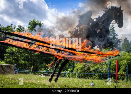 Neu Damerow, Deutschland. 27. Juni 2023. Der 72-jährige „professionelle Indianer“ Wolfgang Kring springt mit seinem Pferd über ein brennendes Hindernis während des Trainings für die jetzt 30. Apache Live Show. Auf der natürlichen Bühne im Mecklenburger Seengebiet feiert das aktuelle Stück seine Premiere am letzten Wochenende im Juli. An insgesamt drei Wochenenden sind insgesamt sechs Vorstellungen mit rund 30 Amateurdarstellern geplant. Die fiktive Geschichte spielt in der Zeit des beginnenden Amerikanischen Bürgerkriegs in der Mitte des 19. Jahrhunderts. Kredit: Jens Büttner/dpa/Alamy Live News Stockfoto