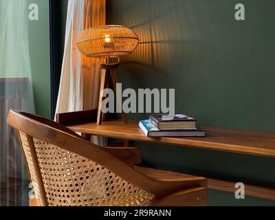 Tischleuchte mit Rattanschirm auf Holztisch mit Rattanstuhl Nahaufnahme Stockfoto