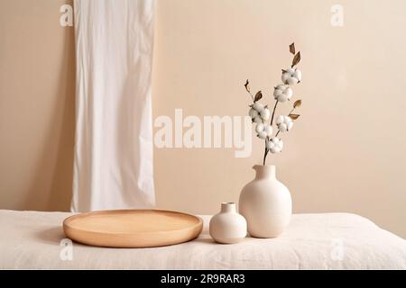 Beige Keramikvasen mit trockenen Baumwollzweigen. Eleganter und minimalistischer Hintergrund für die Präsentation Ihrer Produkte im Wohnzimmer. Skandinavisches Interieur. Moderne Inneneinrichtung. Speicherplatz kopieren. Stockfoto