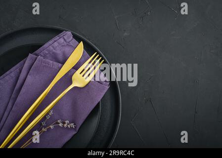 Moderne, minimale Tischplatzierung mit schwarzen Tellern und goldenem Besteck auf schwarzem Hintergrund, Draufsicht. Platz für Text . Moderne Küche. Stockfoto