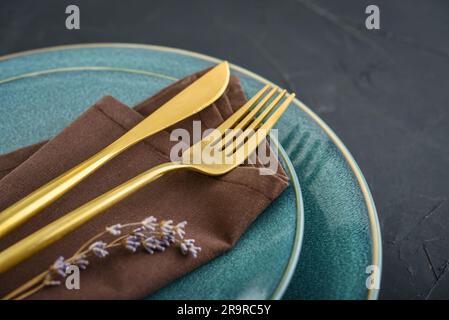 Moderne, kleine Tischaufstellung mit blauen Tellern und goldenem Besteck auf schwarzem Hintergrund. Moderne Küche. Stockfoto