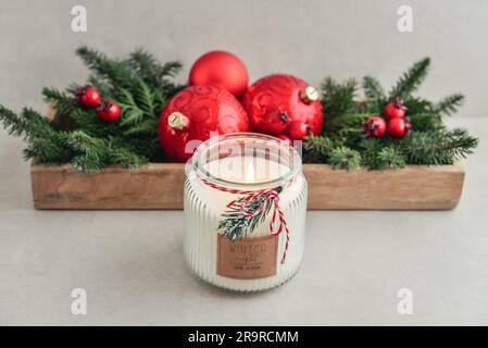 Kerze im Glas mit weihnachtsdekorationen aus Tannenzweigen und roten weihnachtskugeln auf hellem Hintergrund Stockfoto