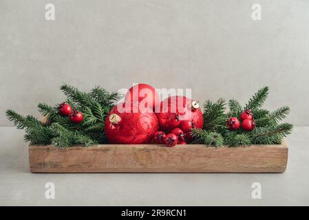 Weihnachtsdekorationen aus Tannenzweigen und roten weihnachtskugeln in Holzkiste auf hellem Hintergrund Stockfoto