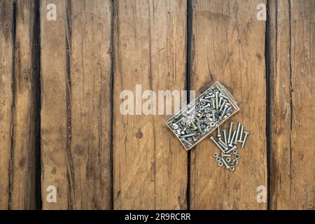 Stahlmuttern und -Bolzen in transparentem Kasten auf dem Holzboden. Schrauben. Holzhintergrund. Stockfoto