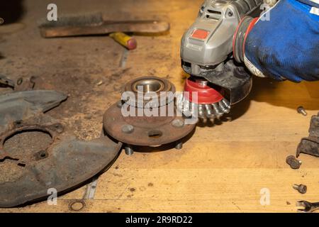 Der Automechaniker reinigt die Radnabe mit einem Winkelschleifer von Rost. Stockfoto