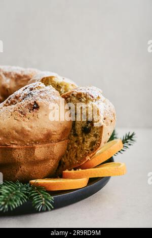 Hausgemachter gebündelter Kuchen mit weißem Zuckerpulver, Orangenlappen und Tannenzweigen auf schwarzem Teller auf hellem Hintergrund Stockfoto