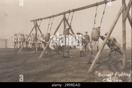 Bajonettkampf in Chatham: Foto aus der Zeit des Ersten Weltkriegs von britischen Soldaten, die Hand-zu-Hand-Kämpfe praktizieren. Auf dem Foto sehen Sie vier Männer, die Bajonette in Sandsäcke rasten, während der Rest der Einheit und zwei uniformierte Sergeants zusehen Stockfoto