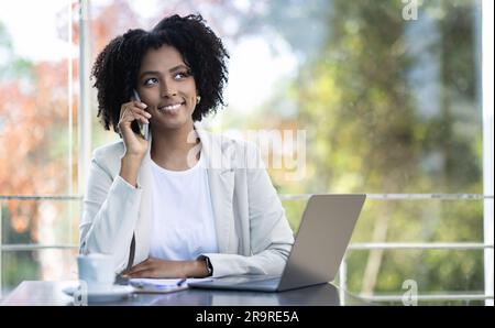 Eine positive, ziemlich schwarze Geschäftsfrau, die telefoniert, im Café arbeitet Stockfoto