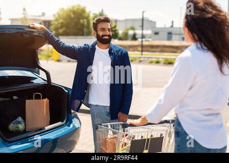 Glückliches arabisches Paar mit einem Einkaufswagen voller frischer Lebensmittel, das Produkte auf dem Außenparkplatz in das Auto packte Stockfoto