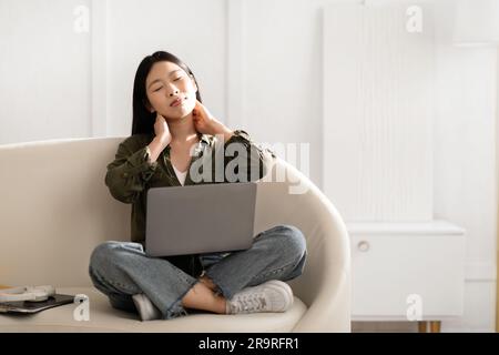 Müde, junge asiatische Frau, selbstständige Unternehmerin, massiert sich den Hals Stockfoto
