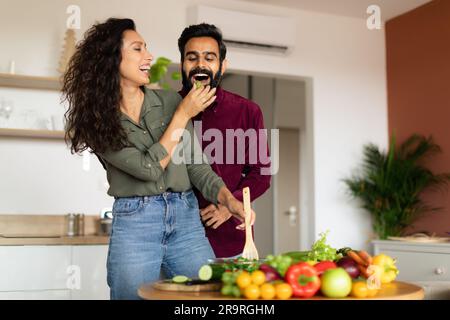 Glückliche, liebende araberin, die Salat schneidet und ihren Mann füttert, in der Küche, im Kopierraum Stockfoto