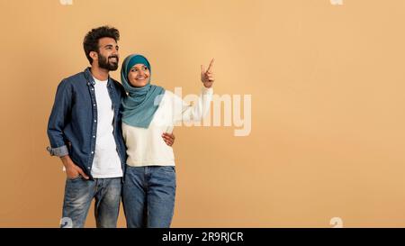 Platz Für Werbung. Glückliches muslimisches Paar, das sich umarmt und auf Kopierraum zeigt Stockfoto