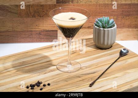 Ein frisch zubereiteter Kaffee martini sitzt auf einem Schneidebrett, begleitet von einer dekorativen saftigen Pflanze Stockfoto