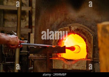 Murano Glasbläserei. Gebläse bildet ein wunderschönes Stück Glas: Legen Sie einen Eisenstab mit befestigtem Glasgegenstand in den Ofen, um das Glas verformbar zu machen. Stockfoto