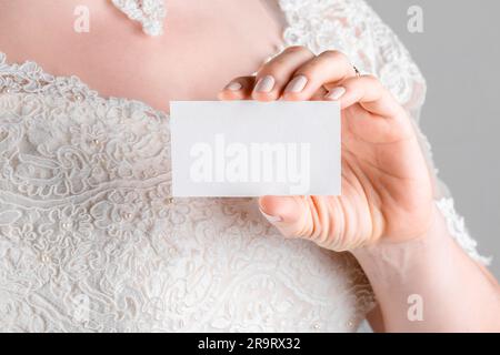 Braut hält Hochzeitsstagionenkarte Modell 2,5 x 3 auf weißem Hintergrund. Minimalistisches, leeres Modell, Dankeskarte, Grußkarte, Hochzeitstempla Stockfoto