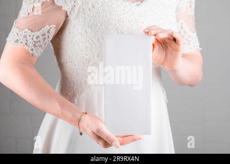 Braut hält Hochzeitsmenü-Kartenmodell auf weißem Hintergrund. Minimalistisches, leeres Modell, Dankeskarte, Grußkarte, Hochzeitsvorlage Stockfoto