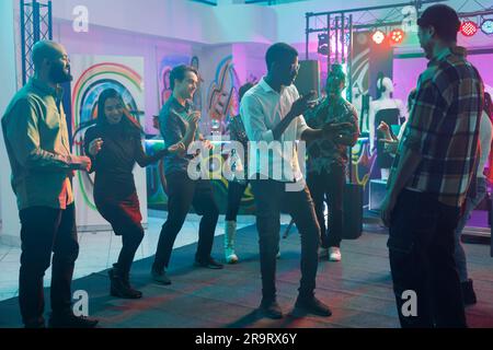 Menschen, die tanzen und feiern, während sie elektronische Musik im Nachtclub genießen. Verschiedene Clubmitglieder haben Spaß und bewegen sich auf der Tanzfläche mit Spotlights, während sie an einer Party im Club teilnehmen Stockfoto