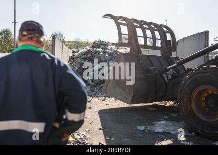 Ein Mitarbeiter des Recyclingzentrums in dunkelblauer Arbeitskleidung, der sich einen unsortierten Müllhaufen ansieht, ist gerade in der Materialrückgewinnungsanlage eingetroffen Stockfoto