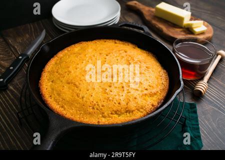 Buttermilch-Maisbrot, gebacken in einer gusseisernen Pfanne in einem niedrigen Winkel: Frisch zubereitetes südliches Maisbrot in einer Pfanne mit Butter und Honig an der Seite Stockfoto