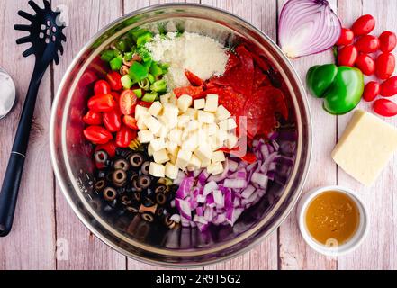 Dreifarbige Nudelsalatgarnituren vor dem Vermischen: Gehacktes und geschnittenes Gemüse und Käse auf Pasta in einer großen Rührschüssel Stockfoto