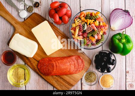 Klassischer Pastasalat Zutaten auf hellem Holzhintergrund: Ungekochte Pasta, Olivenöl, Käse und mehr auf rustikalem Hintergrund Stockfoto
