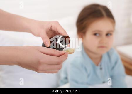 Mutter schüttet Hustensaft in den Messlöffel für ihre Tochter drinnen, konzentriert euch auf die Hände Stockfoto