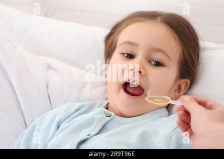 Mutter gibt ihrer Tochter Hustensaft im Schlafzimmer Stockfoto