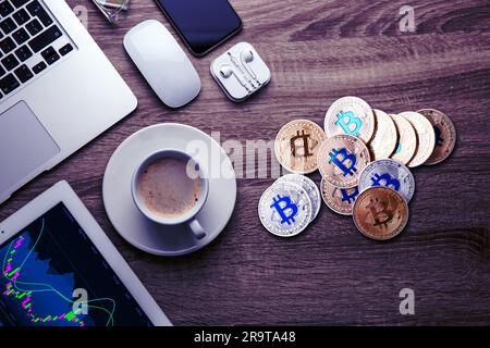 Bitcoins, eine Tasse Kaffee und verschiedene Geräte auf einem Holztisch, flach liegend Stockfoto