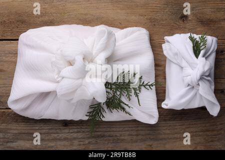 Furoshiki-Technik. Geschenke verpackt in weißem Stoff und Thuja-Äste auf Holztisch, flach liegend Stockfoto