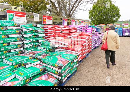 Reife Frau sieht verschiedene Mehrzweckkomposten im Gartenbau verschiedene farbige Kunststoffsäcke, die im Selbstbedienungsbereich Garden Centre Essex England erhältlich sind Stockfoto